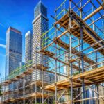 Rugged scaffolding rises high against a clear blue sky, supported by strong metal beams, as a construction project takes shape amidst a bustling urban landscape