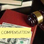 Gavel, cash on a book labeled "COMPENSATION," and stacked books on a black surface.