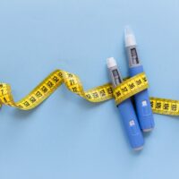 Two blue injection sticks placed on a blue background, showcased next to measuring tape