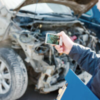 Insurance agent photographing damage after car crash during inspecting damaged automobile for claim form